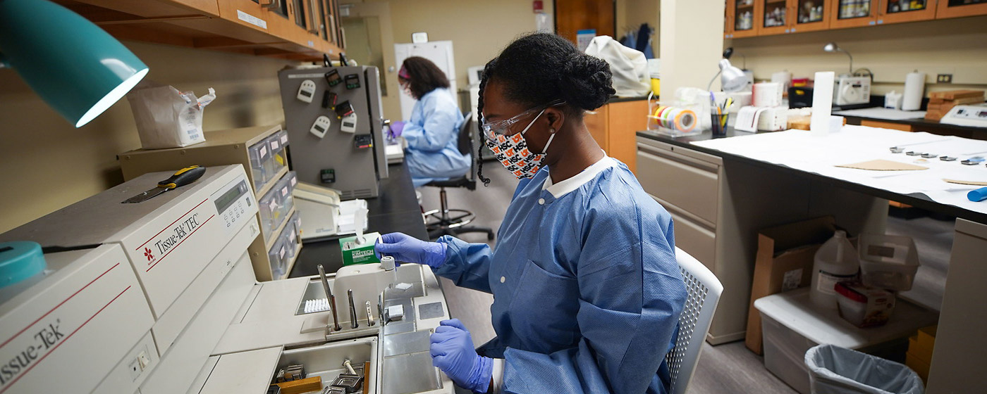 A graduate student wears a face mask, protective eyeware and protective equipment, and prepares to work with live tissue in the cytopathology lab